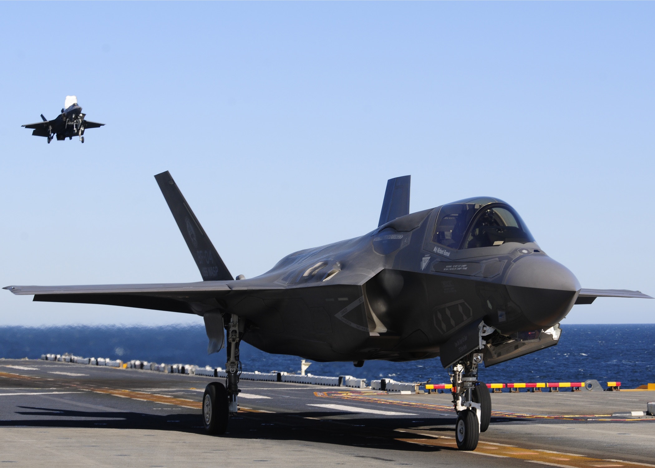 BF-04 maneuvers after a vertical landing as BF-02 (back), the other variant, approaches the flight deck for landing on the amphibious assault ship USS Wasp (LHD 1) on day thirteen of sea trials. The F-35 B was designed to perform STOs and Short Take-Off and Vertical Landing (STOVL) operations on STOVL capable ships and austere airfields. For the USMC, the F-35B will provide air power for the Marine Air Ground Task Force U.S. Navy Photo By Mass Communication Specialist First Class Tommy Lamkin (RELEASED)